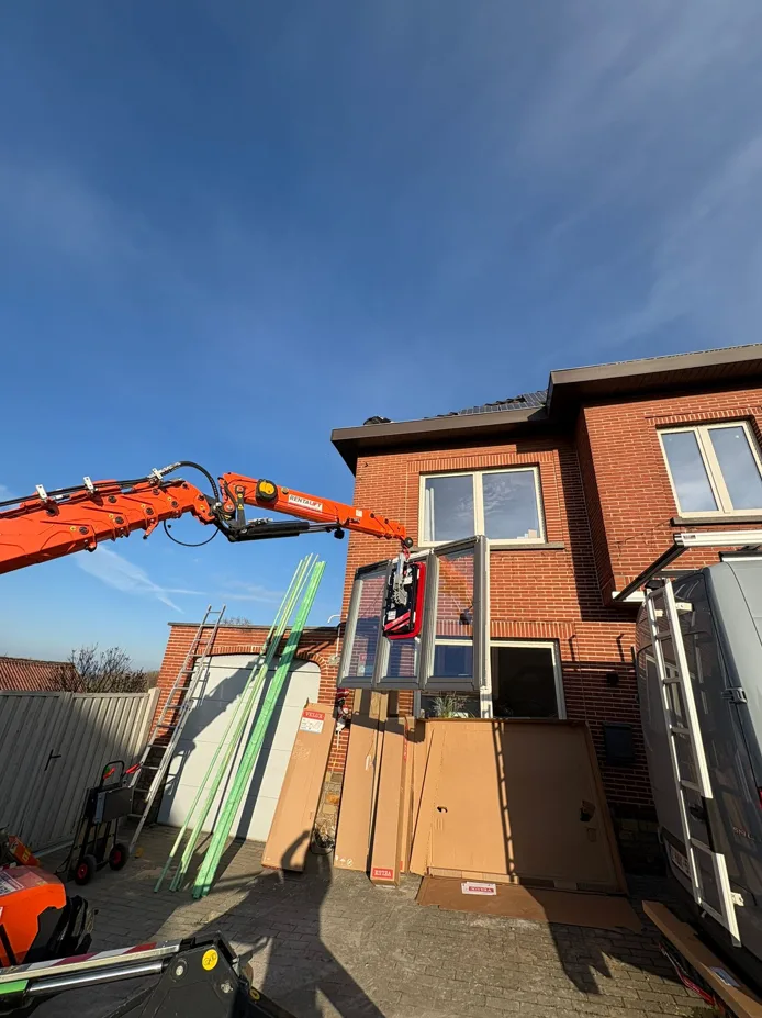 Engin de levage soulevant un ensemble vitré devant une maison en briques