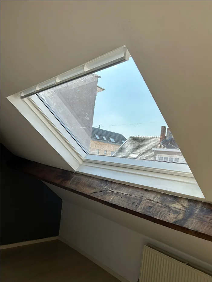 Fenêtre de toit avec encadrement blanc et poutre en bois apparente