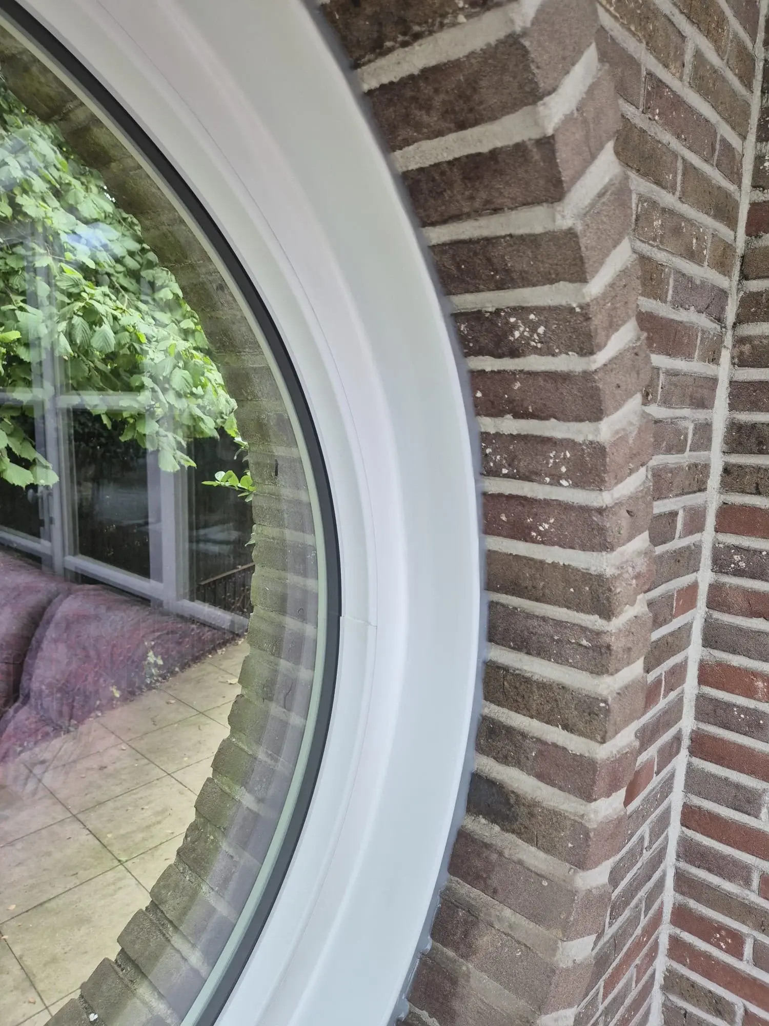 Détail du profilé blanc de la fenêtre ronde sur mesure et de son raccord avec les briques